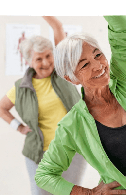 Two Smiling Elderly Women Doing Stretching Exercises at an Independent Living Facility Two Smiling Elderly Women Doing Stretching Exercises at an Independent Living Facility