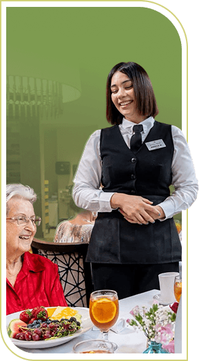 Smiling Female Server Standing beside Seated Elderly Woman at an Independent Living Community