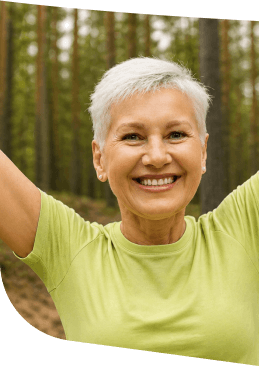 Smiling Elderly Woman with Arms Raised Outdoors among Pine Trees at Independent Living Smiling Elderly Woman with Arms Raised Outdoors among Pine Trees at Independent Living