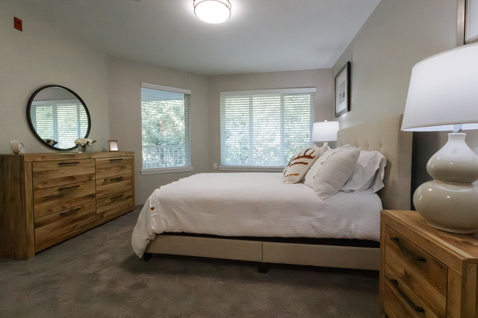 Cozy Furnished Bedroom with Large Windows and Wooden Dresser at an Independent Living Community