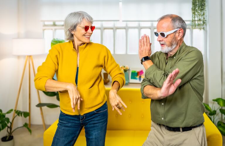 Playful Elderly Couple Dancing Together Wearing Fun Sunglasses Indoors at an Independent Living Facility