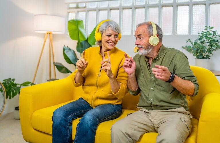 Elderly Couple Wearing Headphones and Dancing Together on a Sofa at an Independent Living Community
