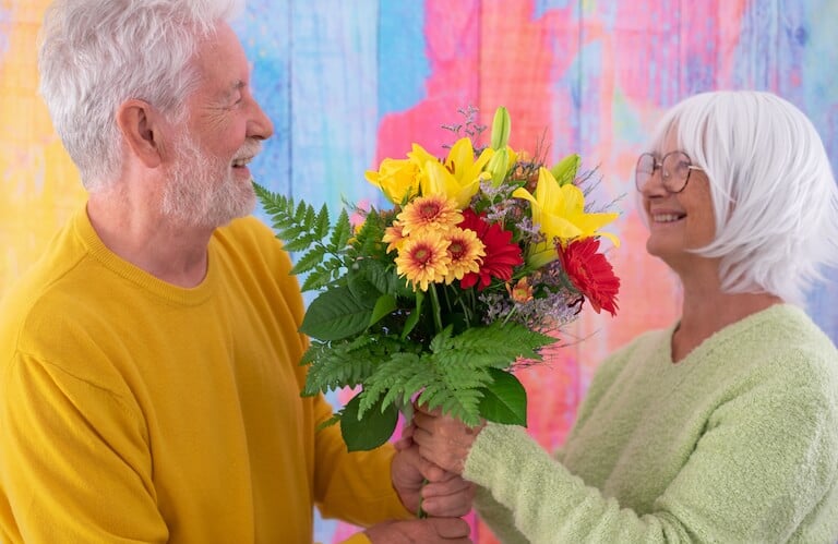 Elderly Man Presenting a Colorful Flower Bouquet to a Smiling Woman at an Independent Living Facility