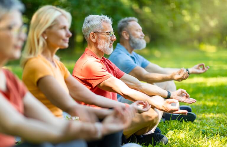 Group of Elderly Residents Practicing Yoga Meditation Outdoors on the Grass at an Independent Living Facility