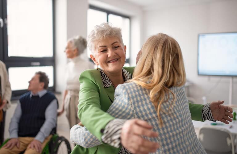 Smiling Elderly Woman Embracing a Friend during a Social Gathering at an Independent Living Facility