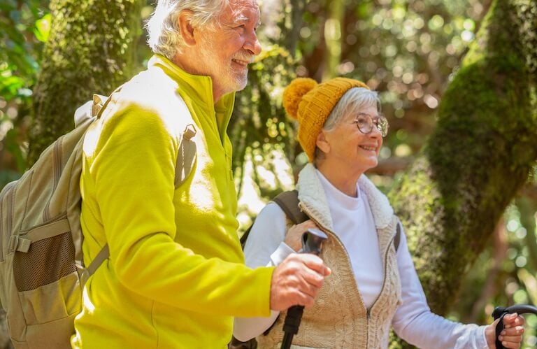 Elderly Couple Hiking Together with Backpacks through a Lush Forest at an Independent Living Community