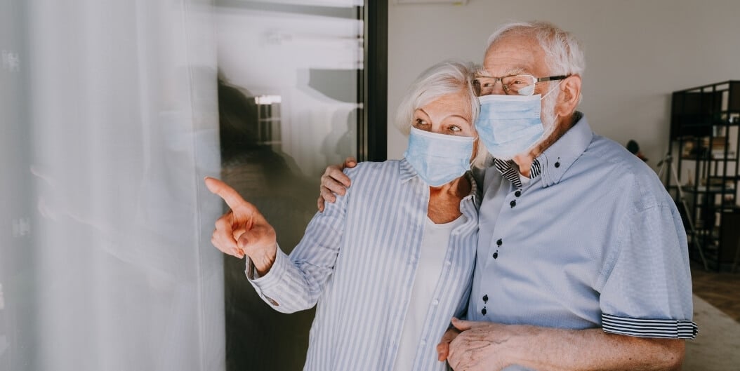 Elderly Couple Wearing Masks Looking out Window at Independent Living Facility